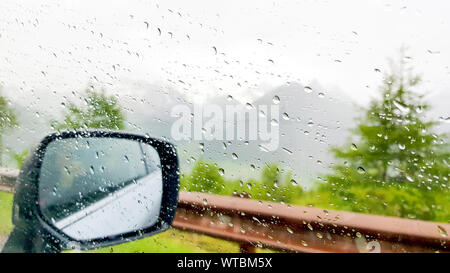 Gouttes de pluie sur la surface de la fenêtre de voiture floue avec vue sur la montagne en arrière-plan, arrière-plan du régime naturel des gouttes. Banque D'Images