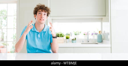 Plan large de jeune homme séduisant à la maison smiling crossing fingers avec espoir et les yeux fermés. Chance et concept superstitieux. Banque D'Images