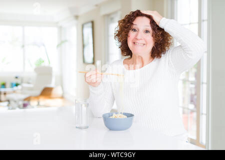 Senior woman eating nouilles asiatiques à l'aide de baguettes a souligné avec la main sur la tête, choqué par la honte et la surprise face, en colère et frustrés. La peur et le haut Banque D'Images
