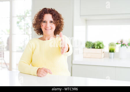 Beau chandail jaune senior woman wearing smiling friendly offrant comme message d'handshake et accueillant. Réussite de l'entreprise. Banque D'Images
