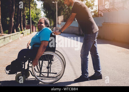 Homme heureux en fauteuil roulant et ami lui en plein air Banque D'Images