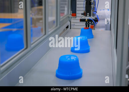 Ligne de production robotisée automatique avec des pots en plastique en mouvement sur convoyeur à bande bleue Banque D'Images