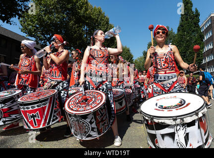 Un groupe de tambours habillés en rouge, blanc et noir costumes imprimés verre bouteilles d'eau qu'ils effectuent à Notting Hill Carnival le 26 août 2019 Banque D'Images