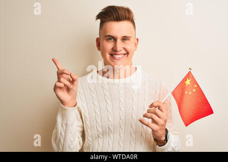 Beau Jeune homme tenant un drapeau Chine chinois isolés sur fond blanc très heureux pointant avec la main et le doigt sur le côté Banque D'Images