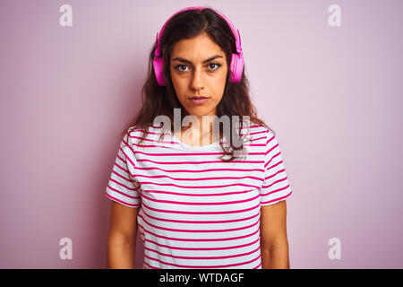 Jeune femme belle écoute de musique à l'aide d'écouteurs sur fond rose isolé avec expression grave sur le visage. Simple et naturelle à Banque D'Images