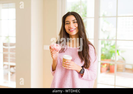 Jeune travailleur woman eating donut rose savoureux et de boire une tasse de café Banque D'Images