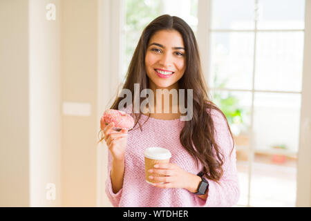 Jeune travailleur woman eating donut rose savoureux et de boire une tasse de café Banque D'Images