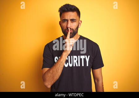 Sauvegarde hispanique indienne arabe homme portant un uniforme de sécurité sur fond jaune isolé demande à être calme avec un doigt sur les lèvres. Silence et secret Banque D'Images