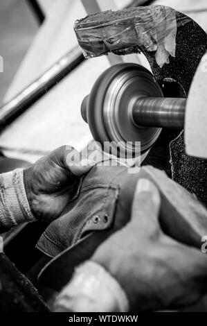 Close up de finition des bords avec des travailleurs de la chaussure de la machine en action dans un atelier avec les mains en noir et blanc Banque D'Images