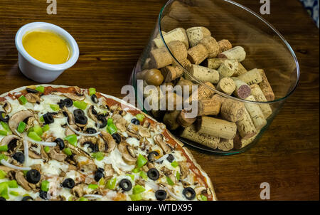 Des yummy pizza aux champignons et poivrons olives fromage servi sur une planche sur une vieille table de cuisine en bois rustique entourée par la sa douce Banque D'Images