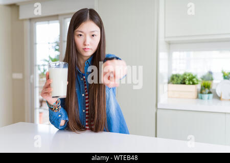 Belle asiatique femme à boire un verre de lait frais avec le doigt pointant à l'appareil photo et à vous, part signe, positif et confiant de la Geste Banque D'Images