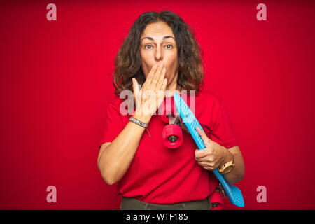 L'âge moyen du patineur senior woman holding skateboard rouge sur fond isolé couvrir la bouche à part choqué avec honte pour l'erreur, d'expression de la fea Banque D'Images