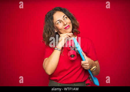 L'âge moyen du patineur senior woman holding skateboard sur fond isolé rouge visage sérieux de penser à question, idée très confus Banque D'Images