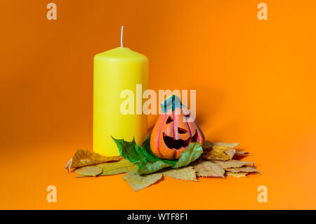 Composition avec céramique décorative Halloween citrouille jack-o-lanterne sur l'automne les feuilles sèches et bougie jaune Banque D'Images