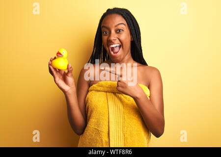 African woman holding serviette de douche canard sur fond jaune isolé très heureux pointant avec la main et des doigts Banque D'Images