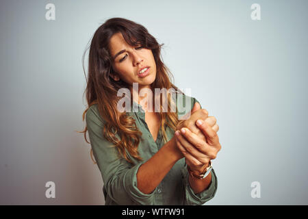 Belle Jeune femme portant chemise verte sur fond gris permanent isolés souffrant de douleur sur les mains et les doigts, l'inflammation de l'arthrite Banque D'Images