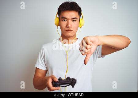 Les jeunes Chinois asiatique gamer man playing video game debout sur fond blanc isolé, visage en colère avec signe négatif montrant non avec thumbs n Banque D'Images