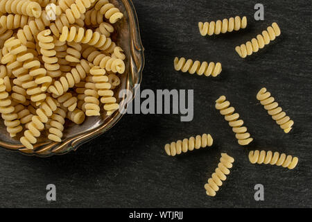 Beaucoup d'entiers et frais fusilli bucati pâtes crues dans le vieux bol de fer flatlay sur pierre gris Banque D'Images