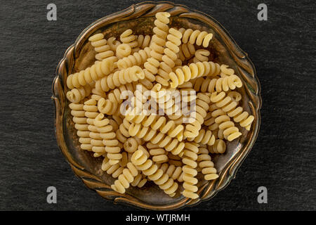 Beaucoup d'entiers et frais fusilli bucati pâtes crues dans le vieux bol de fer flatlay sur pierre gris Banque D'Images