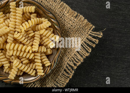 Beaucoup d'entiers et frais fusilli bucati pâtes crues dans le vieux bol de fer sur le tissu du jute sur flatlay pierre gris Banque D'Images