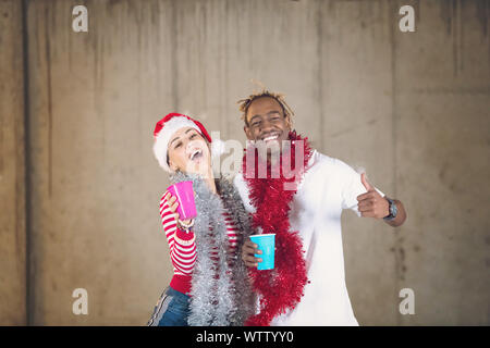 Young casual business couple multiethnique s'amuser tout en célébrant la célébration du nouvel an en démarrage inachevée bureau avec un mur gris derrière eux Banque D'Images