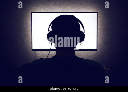 L'homme dans les écouteurs est assis devant un écran vide in dark room Banque D'Images