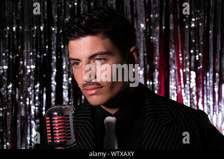 Homme latino attrayant le chant en avant du microphone vintage en boite avec rideau d'argent en arrière-plan Banque D'Images