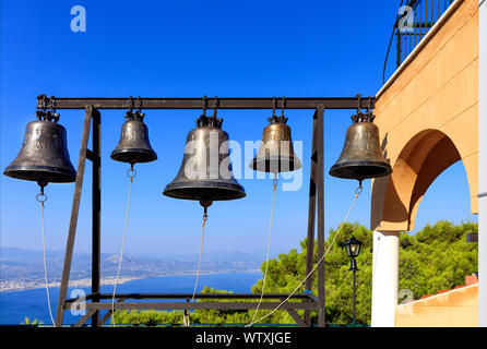 Des cloches de l'Église orthodoxe de Saint-Potapius contre le ciel bleu, la mer Méditerranée et la côte du pin dans le flou, Grèce, Août 2019. Banque D'Images