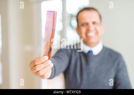 L'âge moyen man holding et montrant peigne à cheveux en souriant à l'appareil photo Banque D'Images