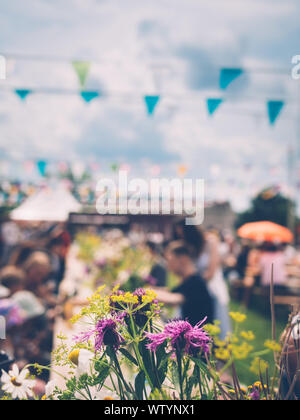 Bouquet de fleurs sauvages, les gens assis à des tables en bois, drapeaux colorés et lumineux sur fond de nuages Banque D'Images