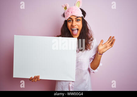 Jeune femme portant un masque de sommeil et de pyjama holding banner sur fond rose isolé très heureux et excité, lauréat expression célébrant la victoire s Banque D'Images