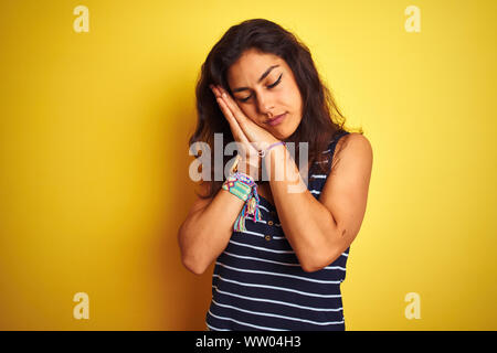 Belle Jeune femme portant un t-shirt à rayures sur fond jaune isolé permanent fatigué dormir rêver et posant avec les mains ensemble tout en sm Banque D'Images