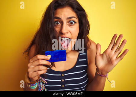 Young Beautiful woman holding credit card debout sur fond jaune isolé très heureux et excité, lauréat expression célébrant la victoire screa Banque D'Images