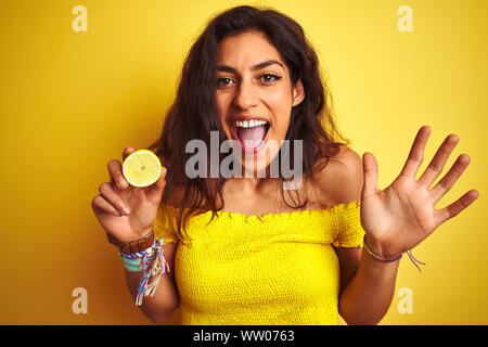 Belle Jeune femme tenant debout au-dessus de citron au fond jaune isolé très heureux et excité, lauréat expression célébrant la victoire scre Banque D'Images