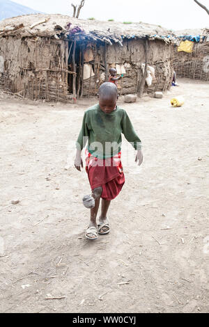 Jeune garçon Maasai jouant au football avec un ballon de fortune dans un kraal en Tanzanie Banque D'Images