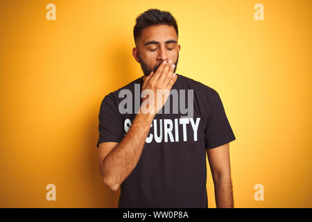 Sauvegarde hispanique indienne arabe homme portant un uniforme de sécurité sur fond jaune isolé ennuyer le bâillement fatigué couvrant la bouche avec la main. Agité et Banque D'Images