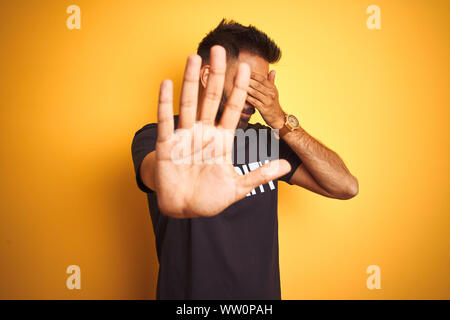 Sauvegarde hispanique indienne arabe homme portant un uniforme de sécurité sur fond jaune isolé couvrant les yeux avec les mains et faire cesser de geste avec une triste Banque D'Images