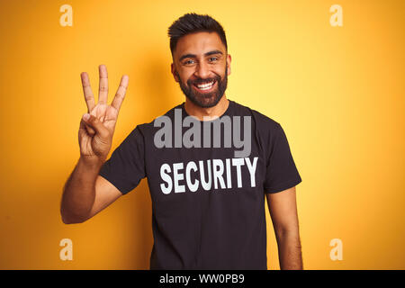 Sauvegarde hispanique indienne arabe homme portant un uniforme de sécurité sur fond jaune isolés montrant et pointant vers le haut avec les doigts tout en numéro trois sm Banque D'Images