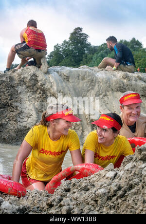 Une équipe de concurrents habillés comme des sauveteurs de Baywatch négocier la 'Mud kilomètre" à la dure épreuve d'endurance en Badminton Mudder Park, Gloucestershire U Banque D'Images