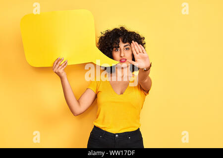 Jeune femme arabe avec des cheveux bouclés holding bulle isolée sur fond jaune avec main ouverte faisant stop avec de sérieux et confiant à l'expre Banque D'Images