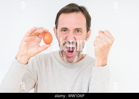 Senior man holding sur fond d'oeufs frais isolé contrarié et frustré de crier avec colère, fou et hurlant de main levée, la colère concept Banque D'Images