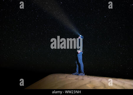 Un homme debout regardant le ciel étoilé avec une lampe de poche, sur une dune dans le désert de l'Erg Chebbi. L'astrophotographie Banque D'Images