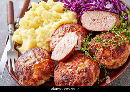 Close-up of crepinette, poêlée de saucisses ou de télévision les galettes de viande hachée et enveloppée de caul gras, servi sur une plaque avec du chou rouge et de purée de sala Banque D'Images