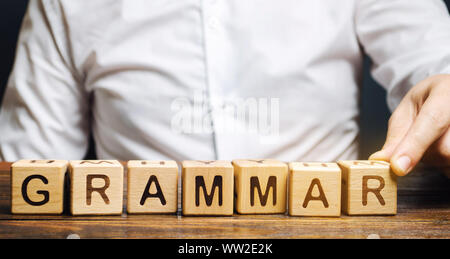 Un homme met des blocs de bois avec le mot grammaire. Ensemble de règles structurelles relatives à la composition des articles, les expressions et les mots dans un langage naturel. Banque D'Images