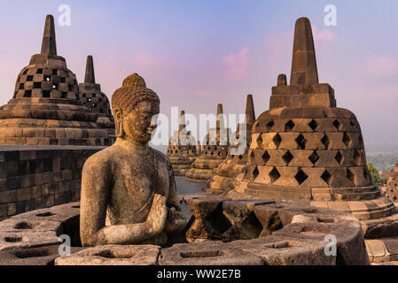 Vue à couper le souffle sur le lever du soleil depuis la statue méditante de Bouddha et les stupas de pierre contre un soleil brillant. L'ancien temple bouddhiste de Borobudur Banque D'Images