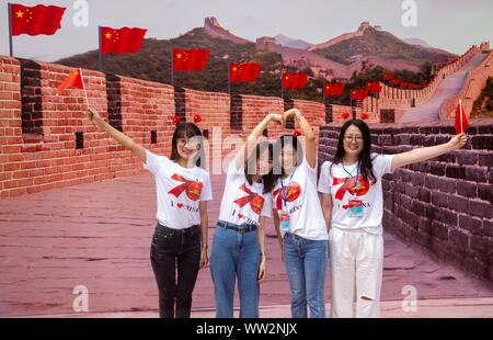 Les jeunes femmes chinoises vague des drapeaux nationaux chinois en face d'une toile montrant le drapeau qui flotte à Great Wall au cours d'une campagne pour célébrer le 70e Banque D'Images