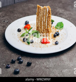 Tranche de gâteau au miel sur une assiette décorée avec des fruits rouges sur fond gris. Banque D'Images