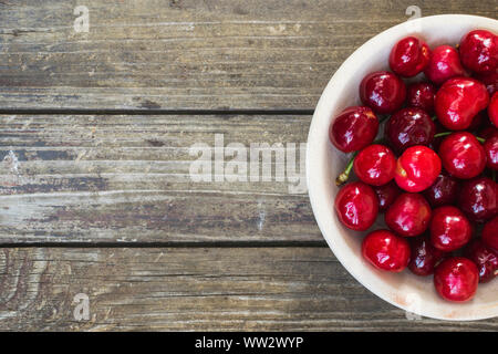 Cerises rouges frais dans un bol sur la table en bois. High angle view Banque D'Images