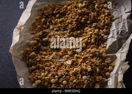 Vue de dessus de granola rôti aux noix, raisins secs et flocons sur le papier parchemin. Texture Close up Banque D'Images