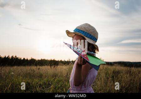 Profil d'une fille jouant avec paper planes au coucher du soleil dans un pré Banque D'Images